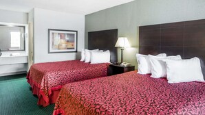 Habitación de hotel con dos camas, un espejo grande, un cuadro enmarcado, una mesita de noche con lámpara y una alfombra verde.