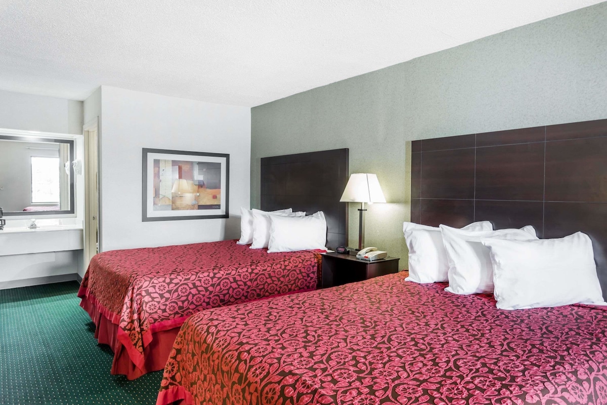 A hotel room with two beds, a nightstand, a lamp, a framed picture, and a window.
