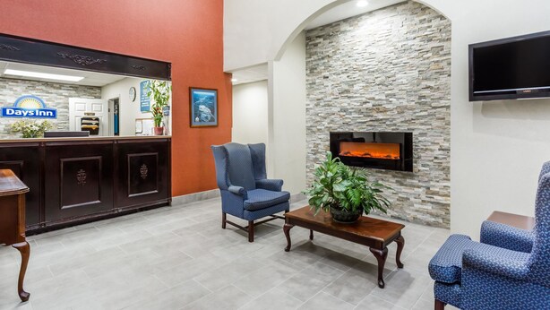 Un área de recepción con un letrero de Days Inn, una pared de piedra con chimenea y dos sillones estampados azules.