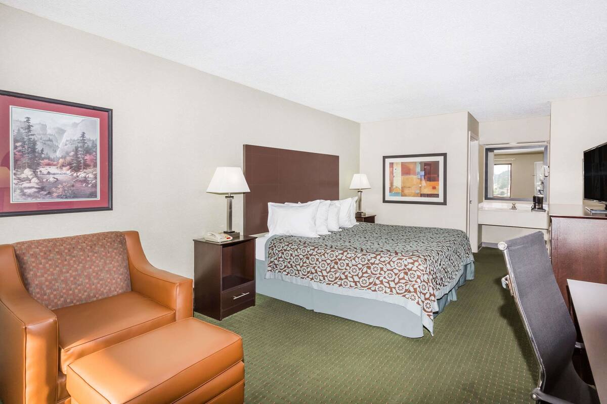A hotel room with a bed, a chair, a desk, a nightstand, and a painting on the wall.