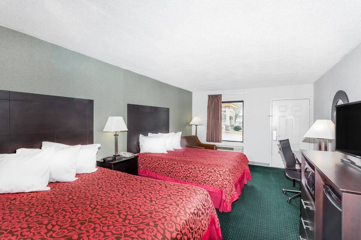 A hotel room with two beds, a desk, a television, and a chair.