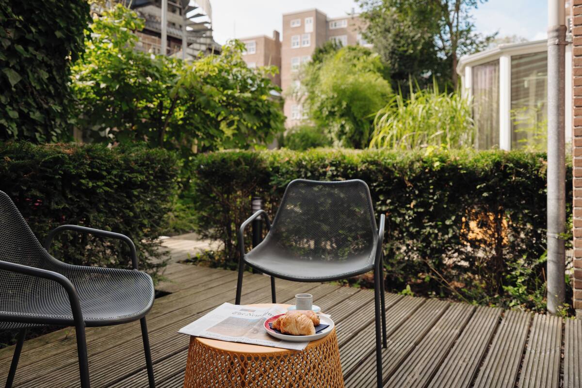 A wooden deck with two chairs and a table, a plate with croissants, and a newspaper.