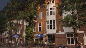 A multi-story building with a brick facade, multiple windows, and a corner section with a white trim. There are bicycles parked outside and a sign indicating a speed limit of 30 km/h. - Conscious Hotel Museum Square (Amsterdam)