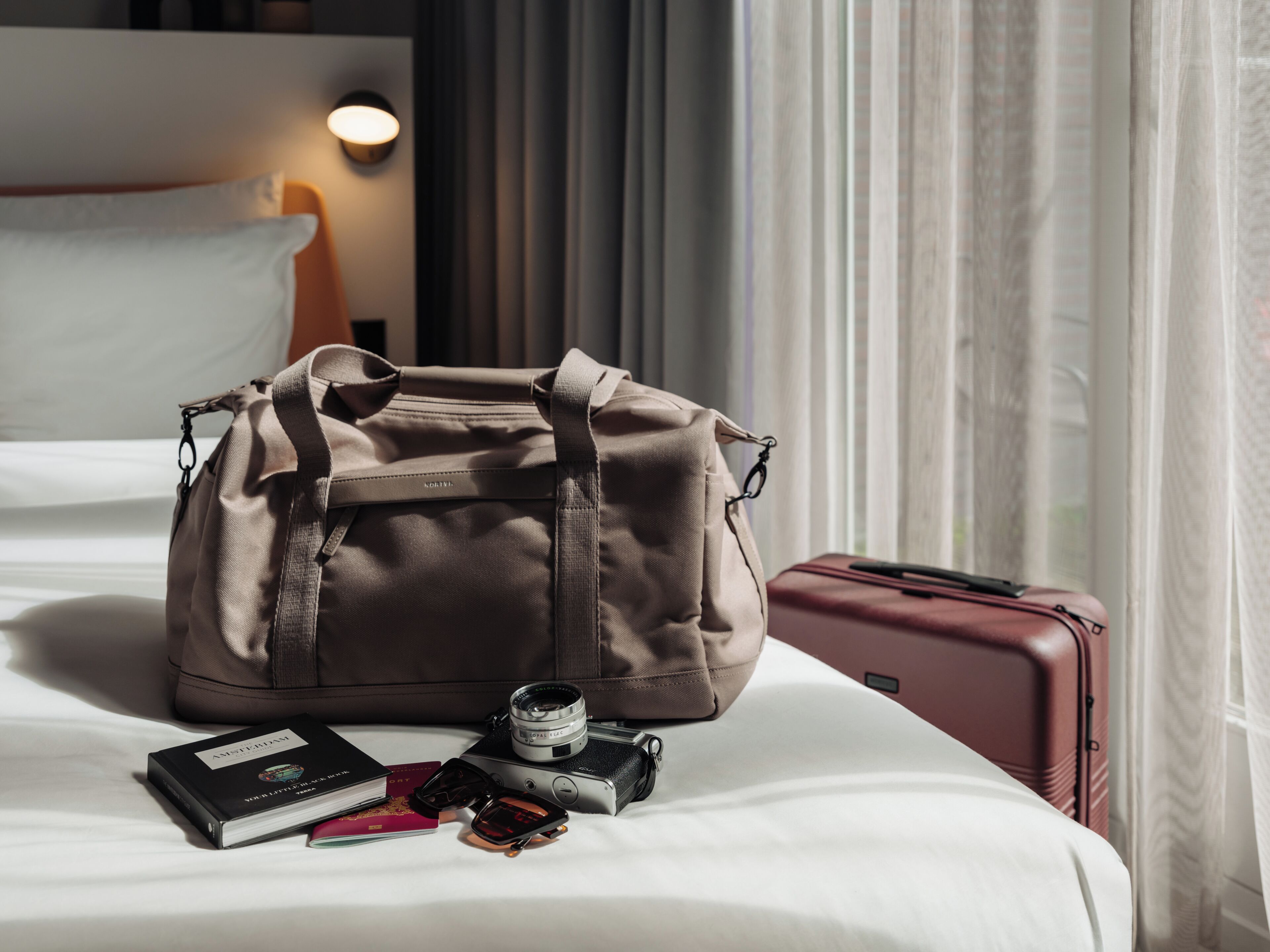 A bed with a large duffel bag, a camera, and a passport on it.