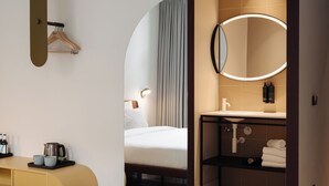 A modern hotel room with a bed, a vanity with a mirror, a coffee machine, and a wardrobe. - Conscious Hotel Museum Square (Amsterdam)