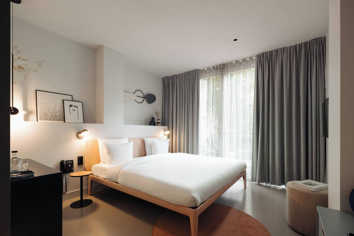 A modern hotel room with a large bed, bedside lamps, a desk with a telephone, and a television on the wall.