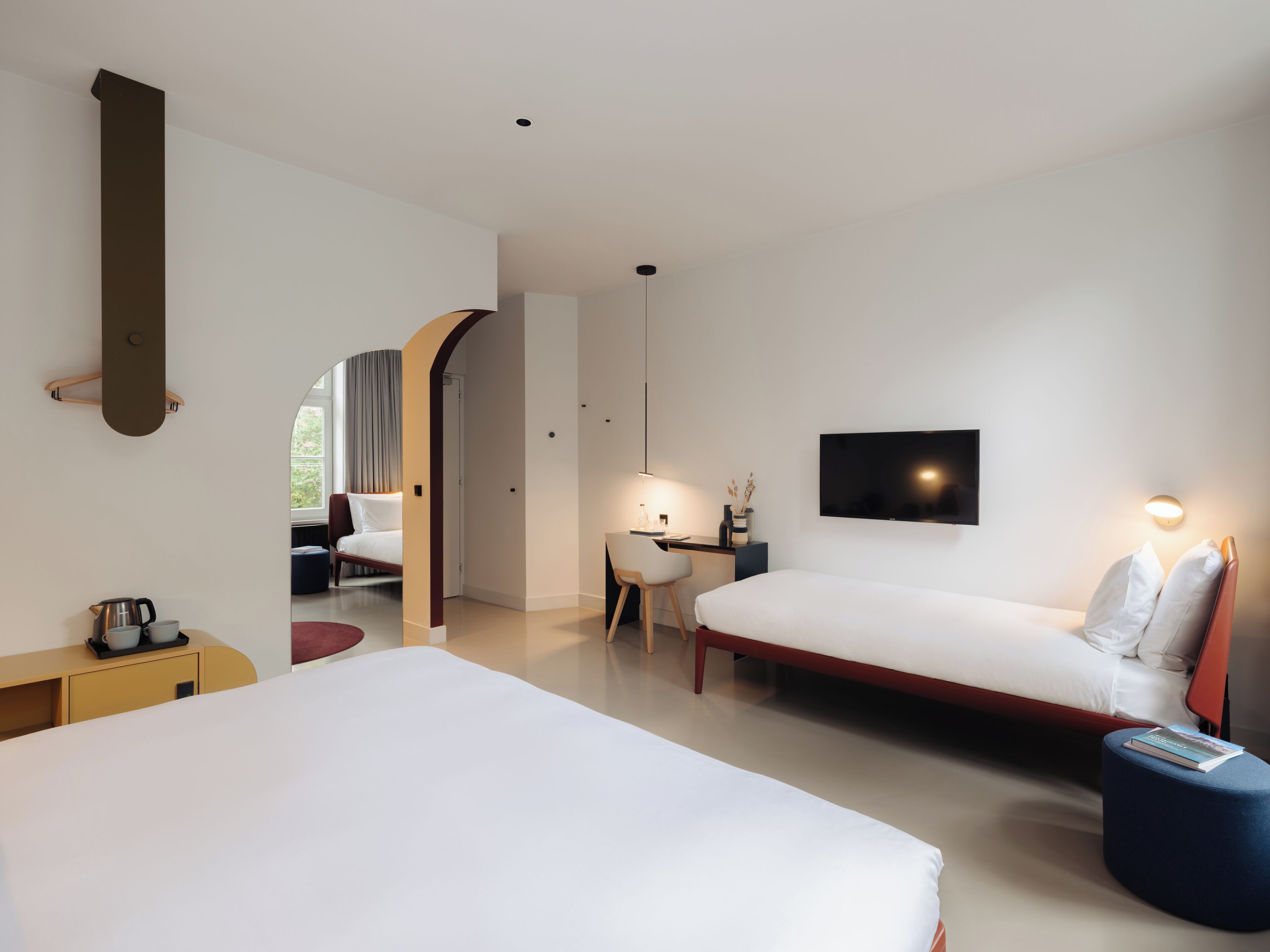 Ein modernes Hotelzimmer mit einem großen Bett, einem Schreibtisch, einem Sessel, einem Fernseher und einem kleinen Tisch mit einem Buch.