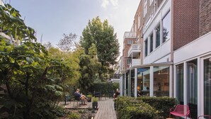 A courtyard with a wooden deck, seating areas, and a large tree. - Conscious Hotel Museum Square (Amsterdam)
