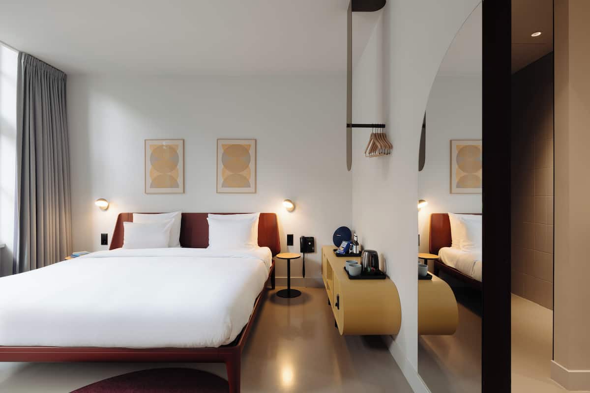 A modern hotel room with a large bed, bedside tables, a mirror, and artwork on the walls.