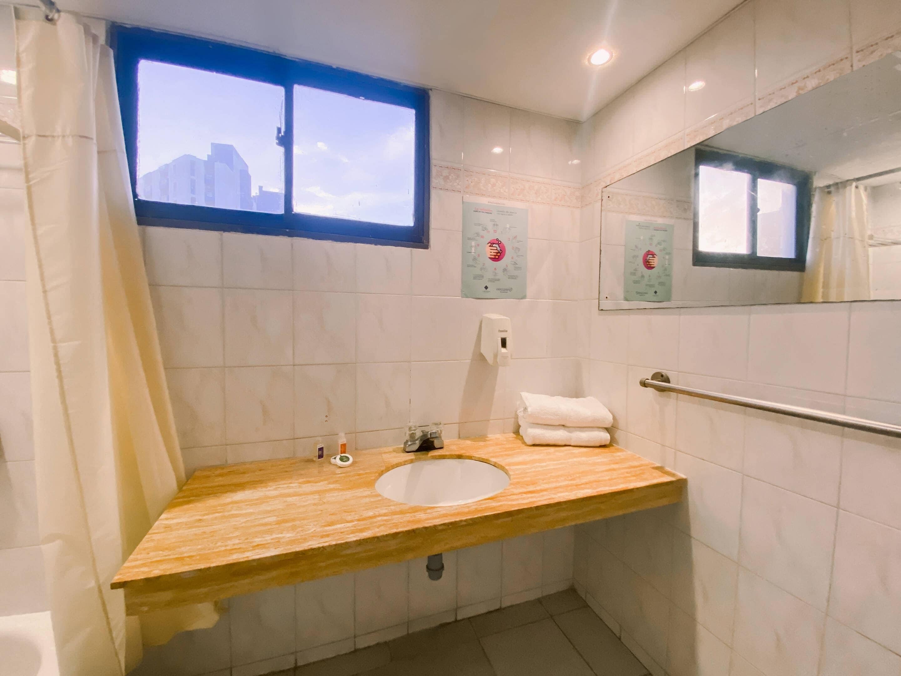 Ein Badezimmer mit einem Holzlagerflächen, einem Waschbecken, einem Fenster und einem Handdesinfektionsmittelspender.