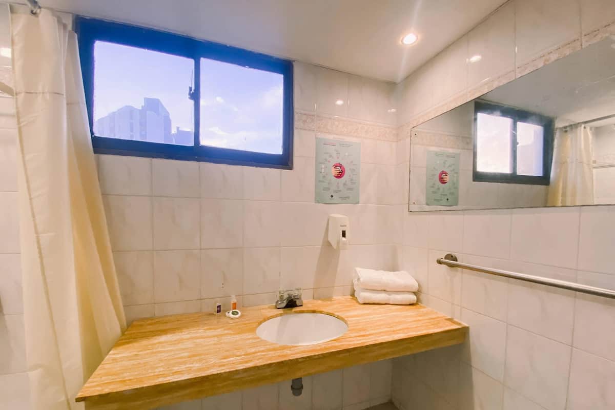Une salle de bain avec un meuble-lavabo en bois, un évier, une fenêtre et un distributeur de gel hydroalcoolique.