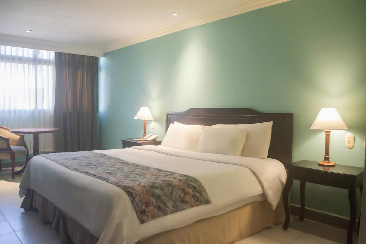 A hotel room with a bed, two bedside tables with lamps, a chair, and a window with curtains.