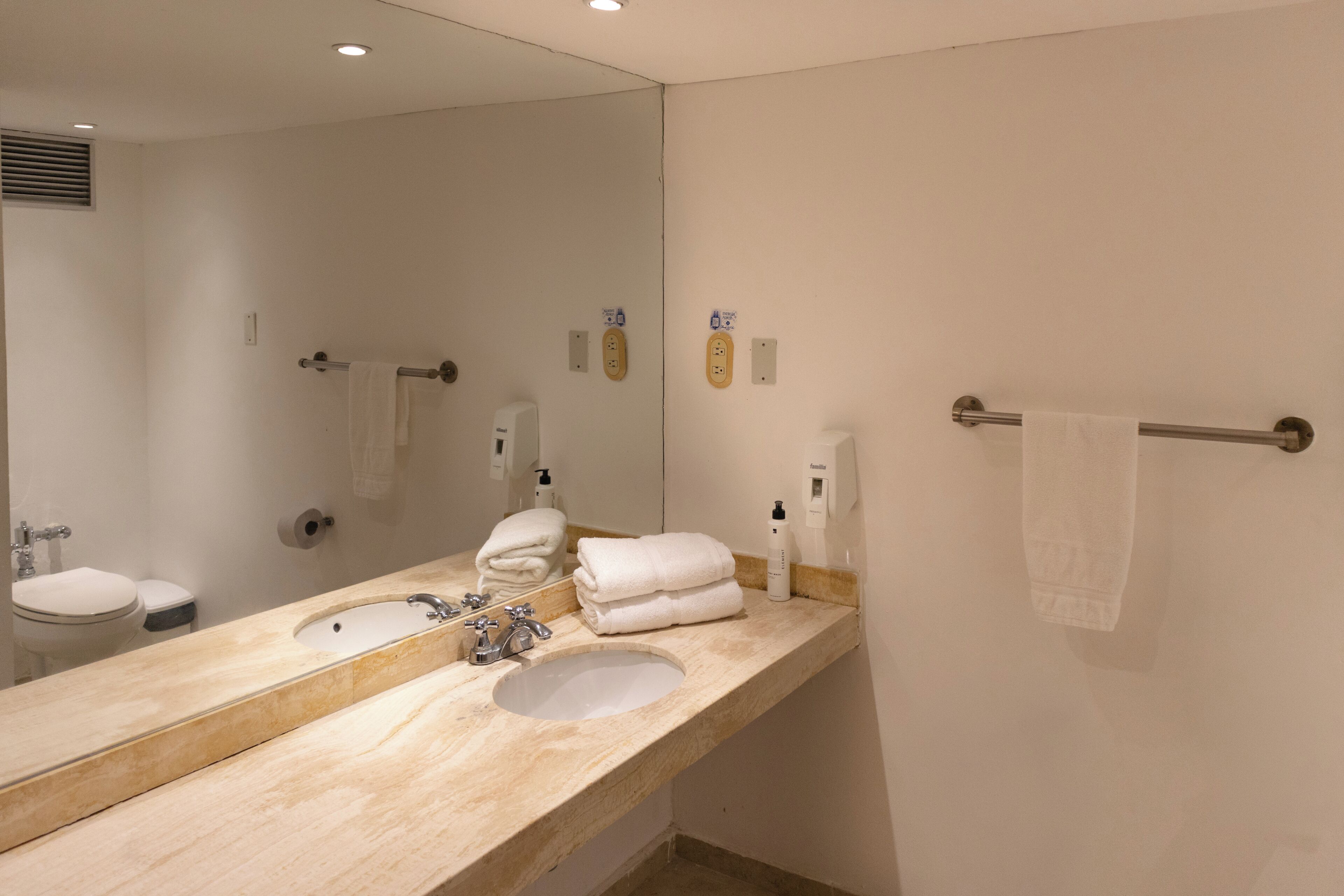 Un baño con lavamanos, espejo, toallero y retrete.