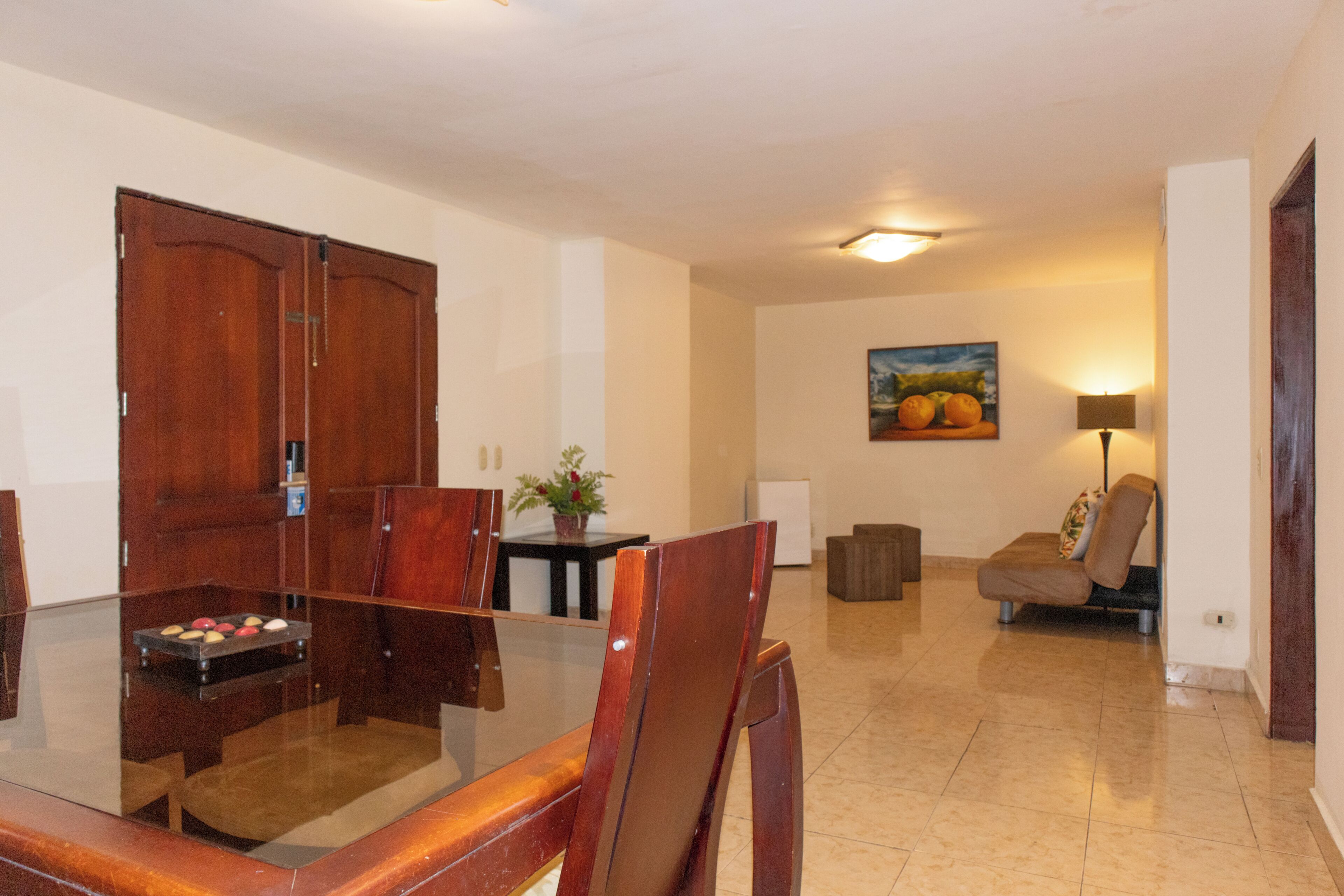 Un comedor con una mesa de vidrio, sillas de madera, un sofá, una lámpara y un cuadro en la pared.
