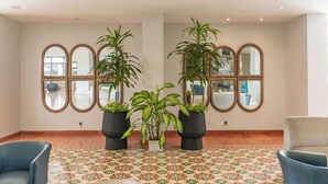 A lobby with a patterned floor, three potted plants, and mirrored wall decorations. - Hotel Faranda Express Puerta Del Sol Barranquilla, A Member of Radisson Individuals (Barranquilla)
