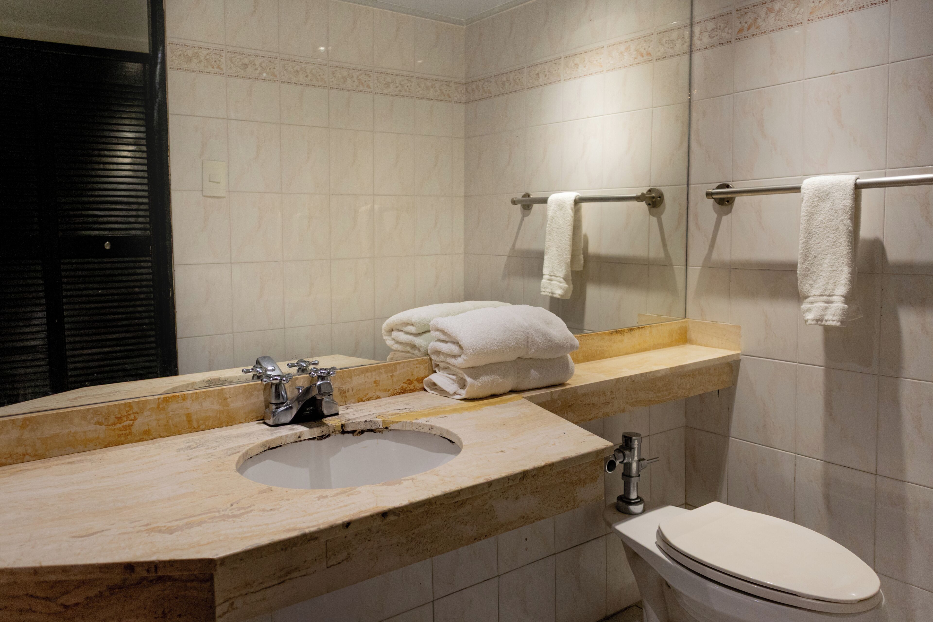 Un baño con lavamanos, espejo, toallero y retrete.