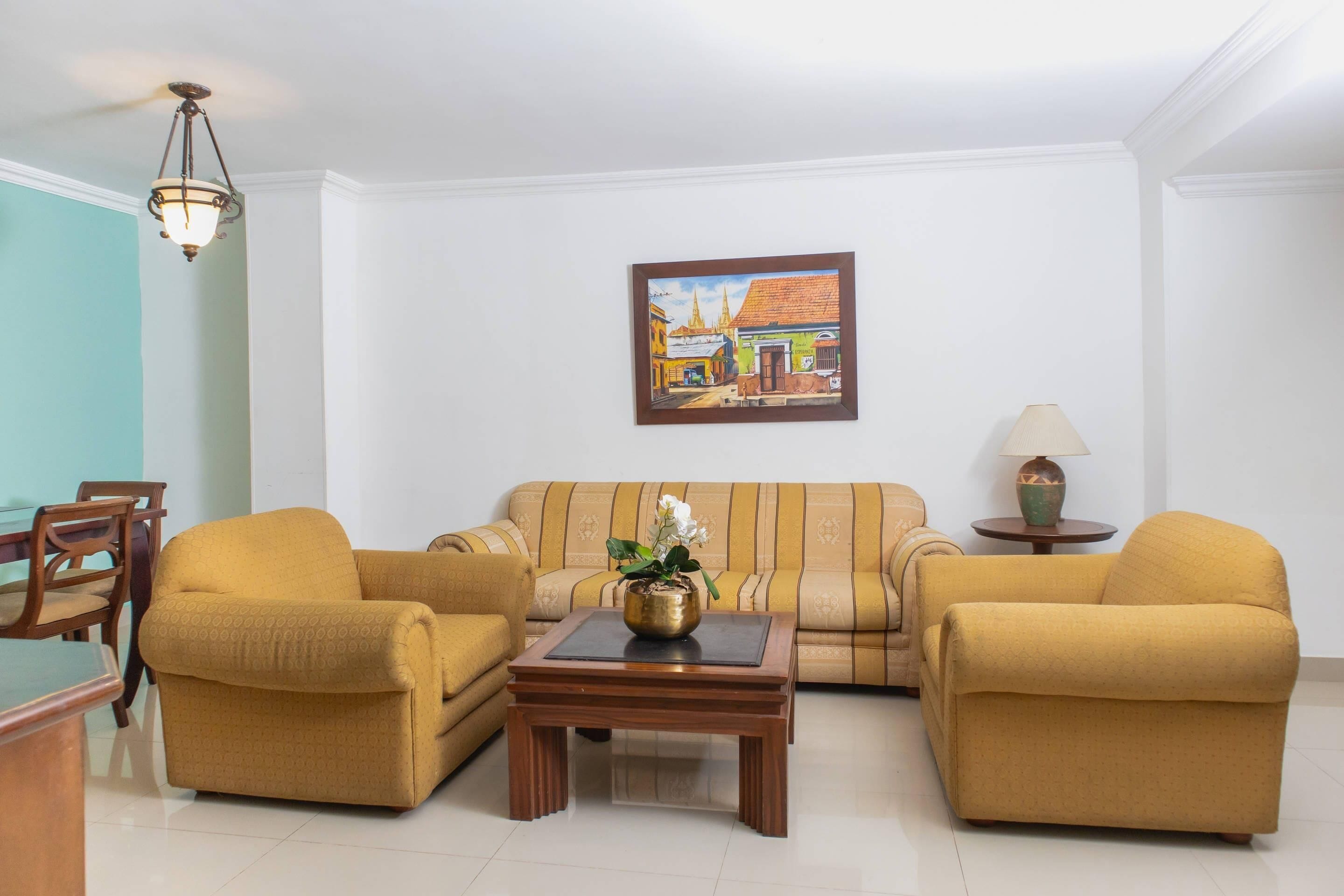 Ein Wohnzimmer mit einer Couch, zwei Sesseln, einem Couchtisch und einem Gemälde an der Wand.