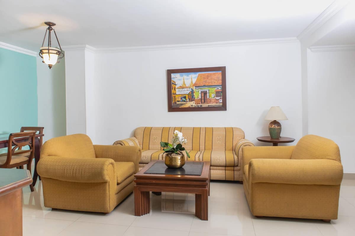 Un salon avec un canapé, deux fauteuils, une table basse et un tableau accroché au mur.