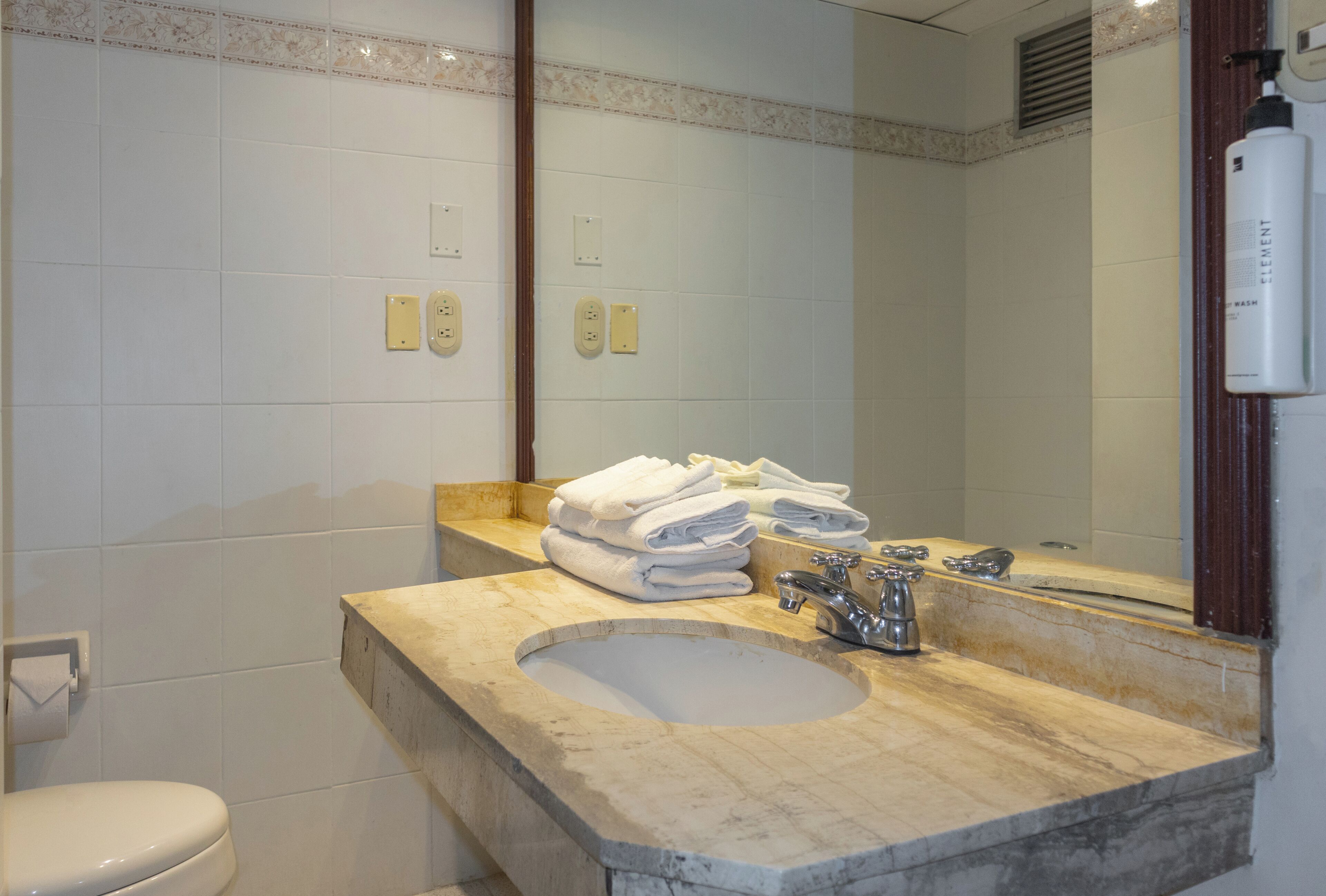 A bathroom with a marble sink, a mirror, and a stack of towels.