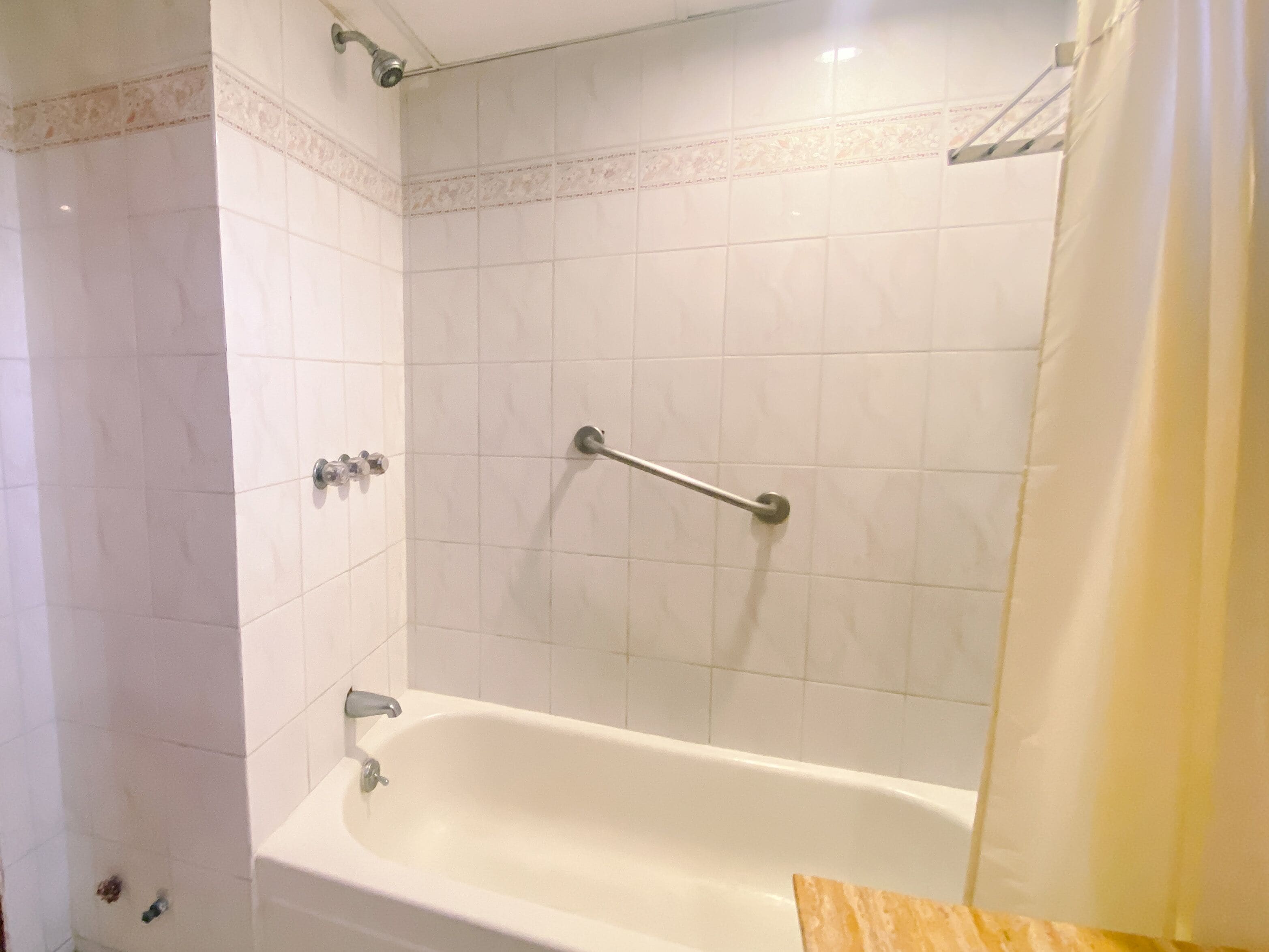 A bathroom with a bathtub, a shower, and a handrail.