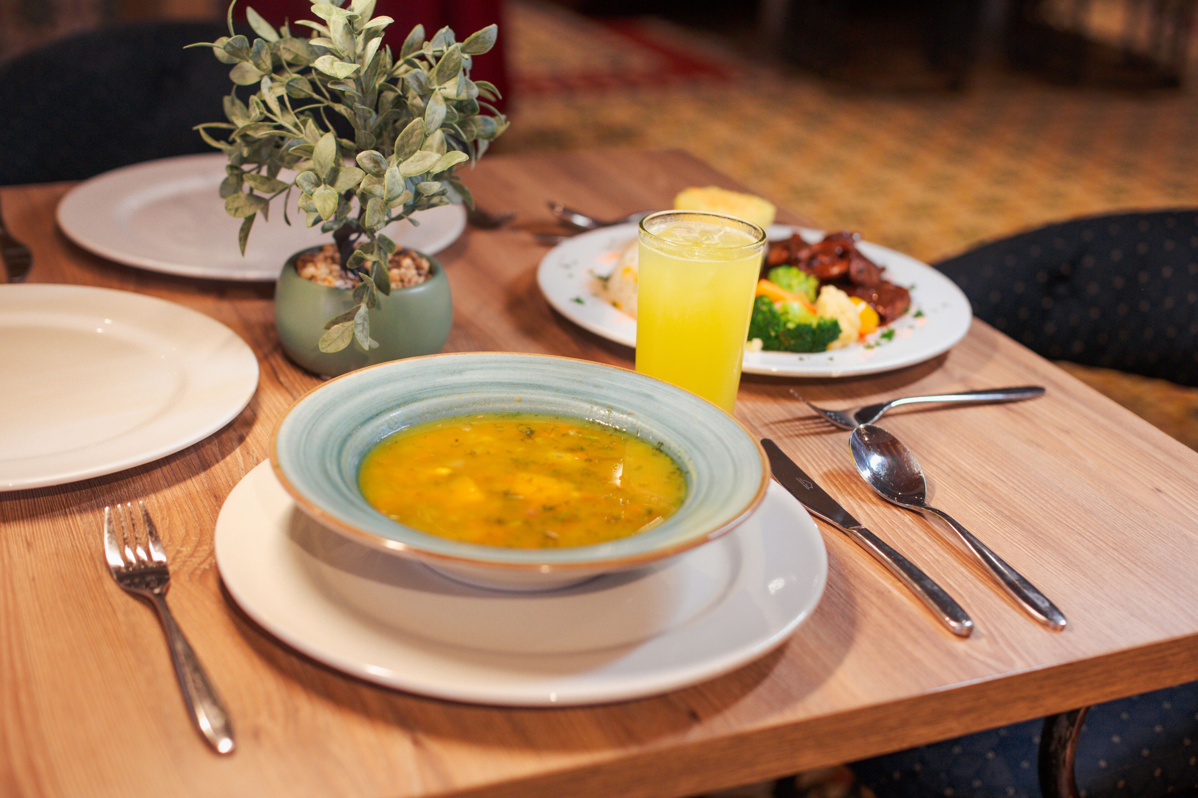 A dining table with a bowl of soup, a glass of orange juice, and plates of food.
