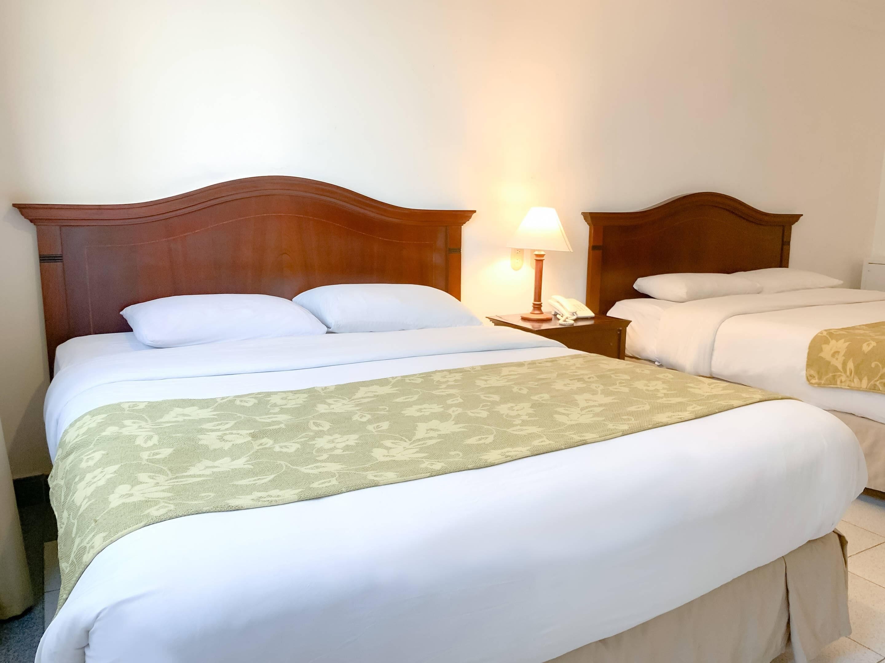 Ein Hotelzimmer mit einem großen Bett, einem Nachttisch mit Lampe und einem Telefon.
