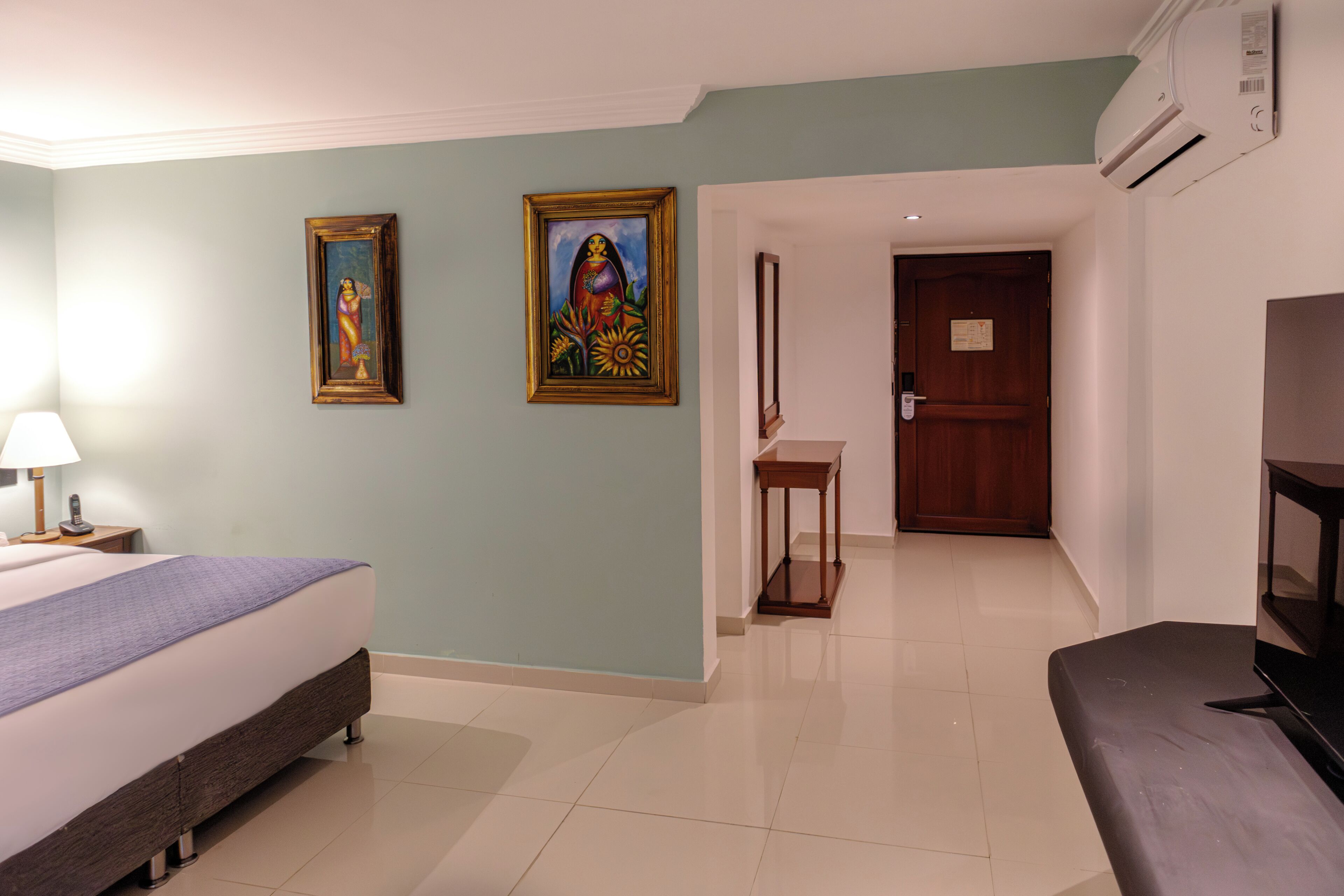 Una habitación de hotel con cama, televisión, escritorio y dos cuadros en la pared.