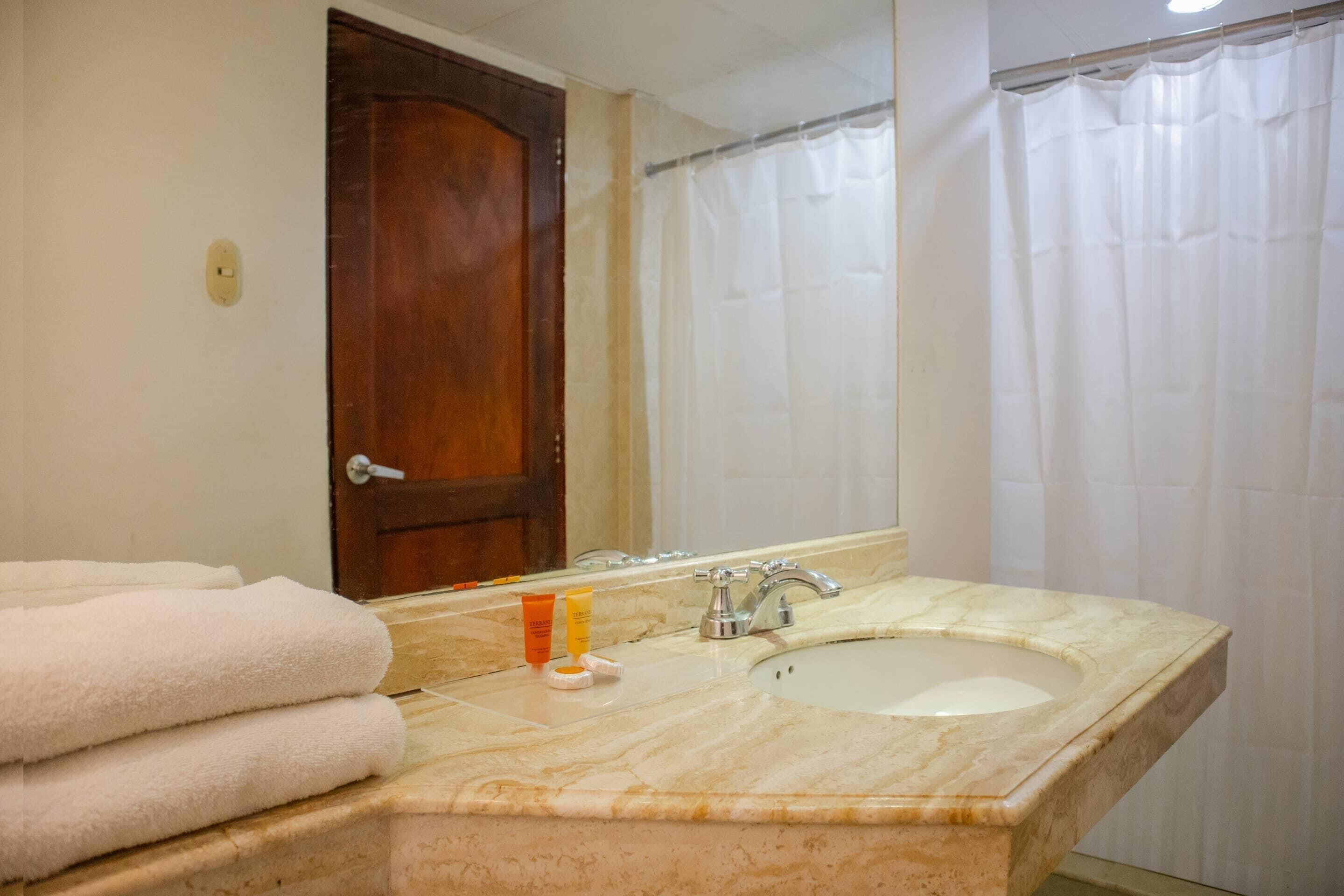 A bathroom with a marble sink, a mirror, a wooden door, and a shower curtain.