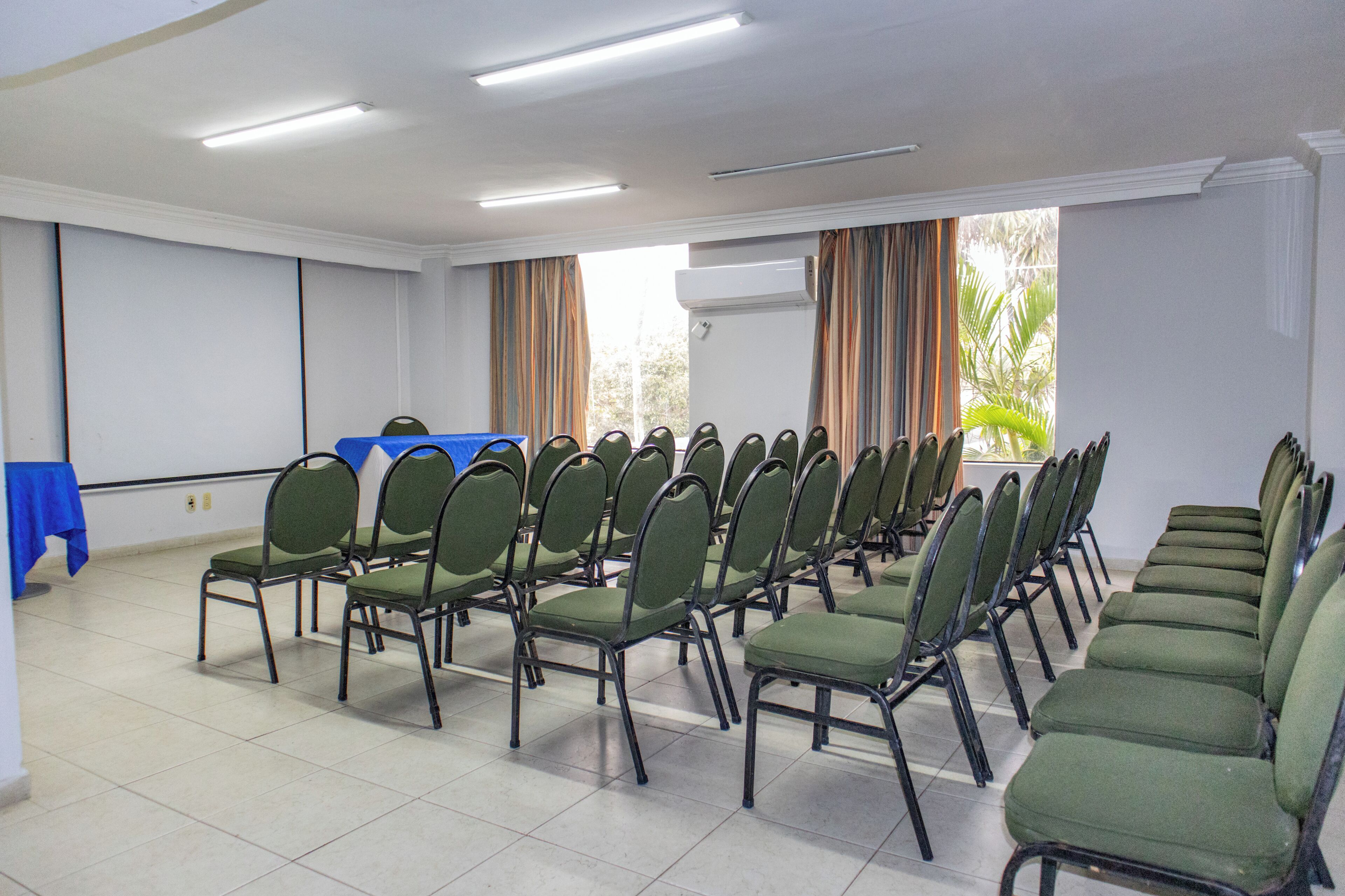 A conference room with rows of green chairs, a blue table, and a large window with curtains.
