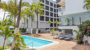 A pool area with lounge chairs, palm trees, and a modern building with balconies. - Hotel Faranda Express Puerta Del Sol Barranquilla, A Member of Radisson Individuals (Barranquilla)