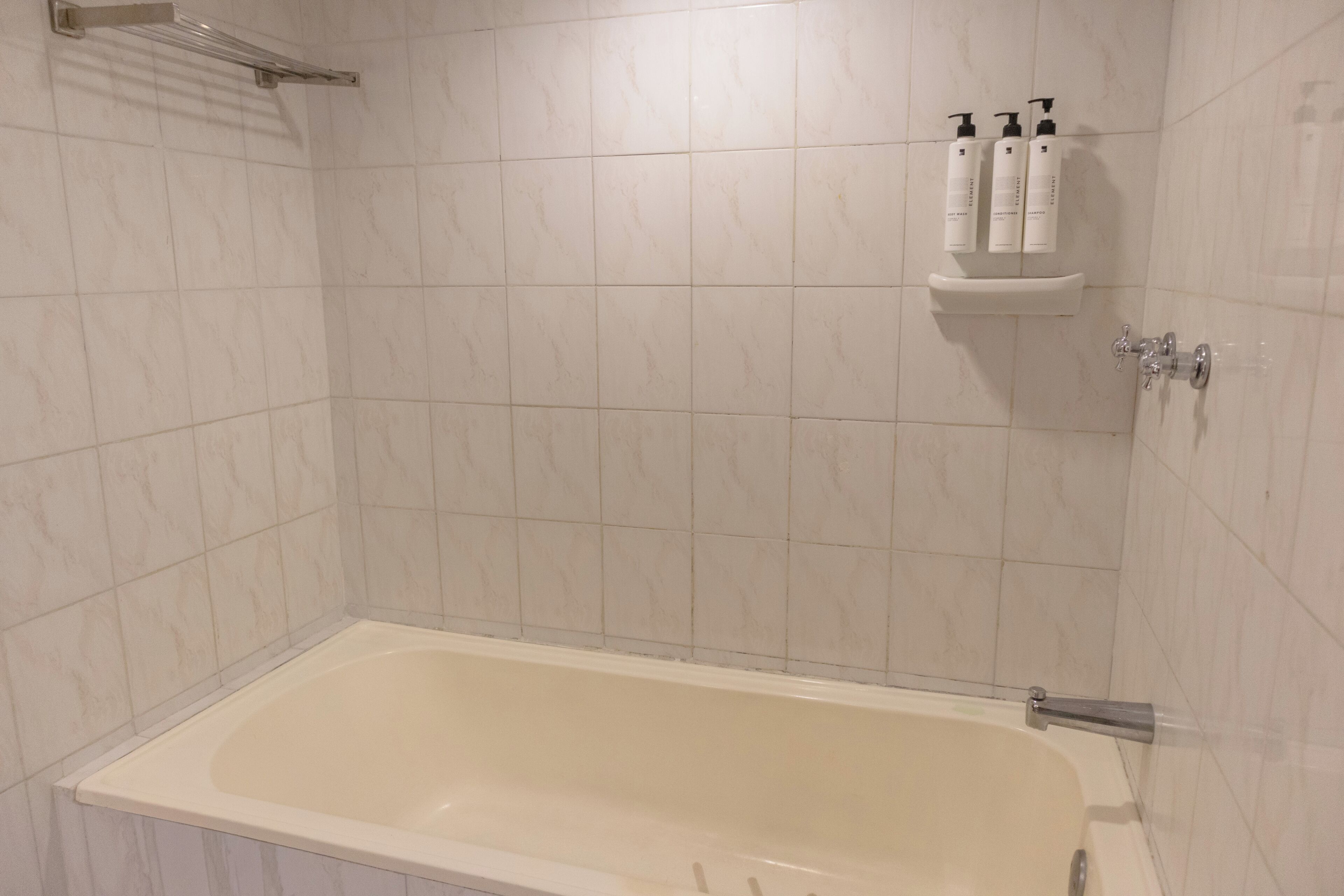 A bathroom with a bathtub, a shower area, and a shelf with toiletries.