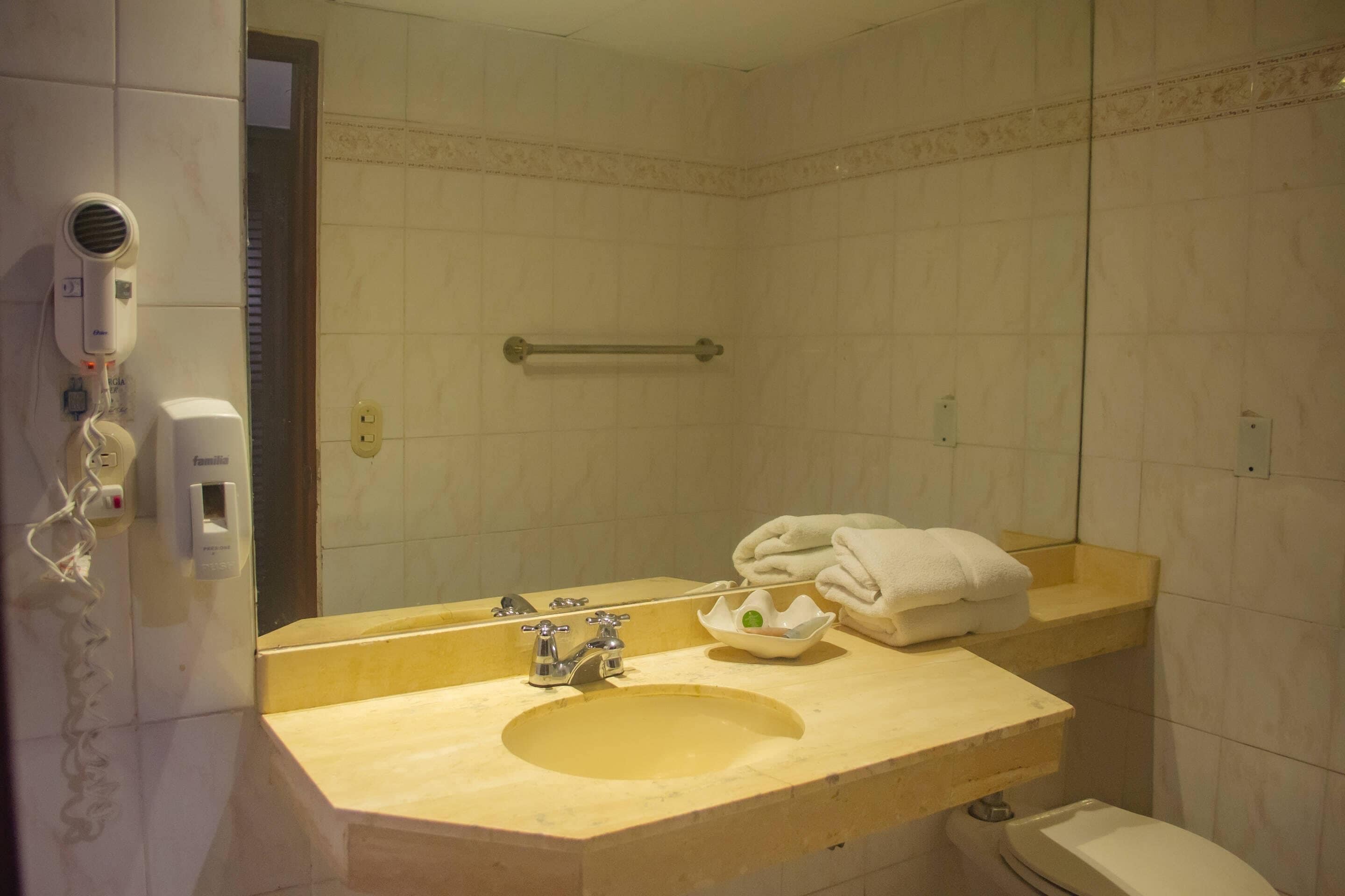 Ein Badezimmer mit Waschbecken, Spiegel, Handtuchhalter und einem Föhn.