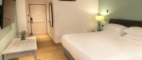 A hotel room with a bed, bedside table, lamp, air conditioning unit, and a door.