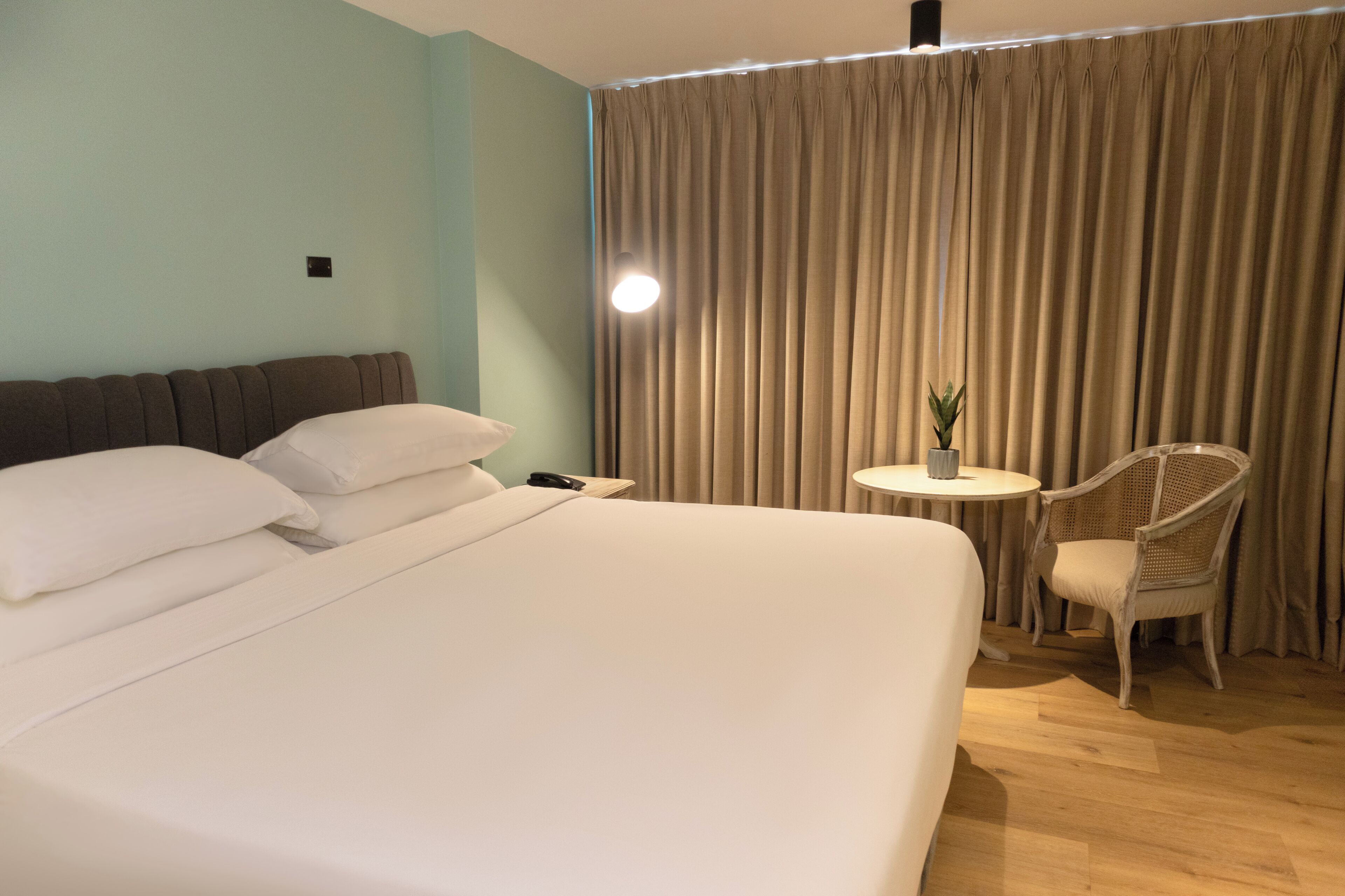 A hotel room with a large bed, a small round table, a chair, and a curtain.