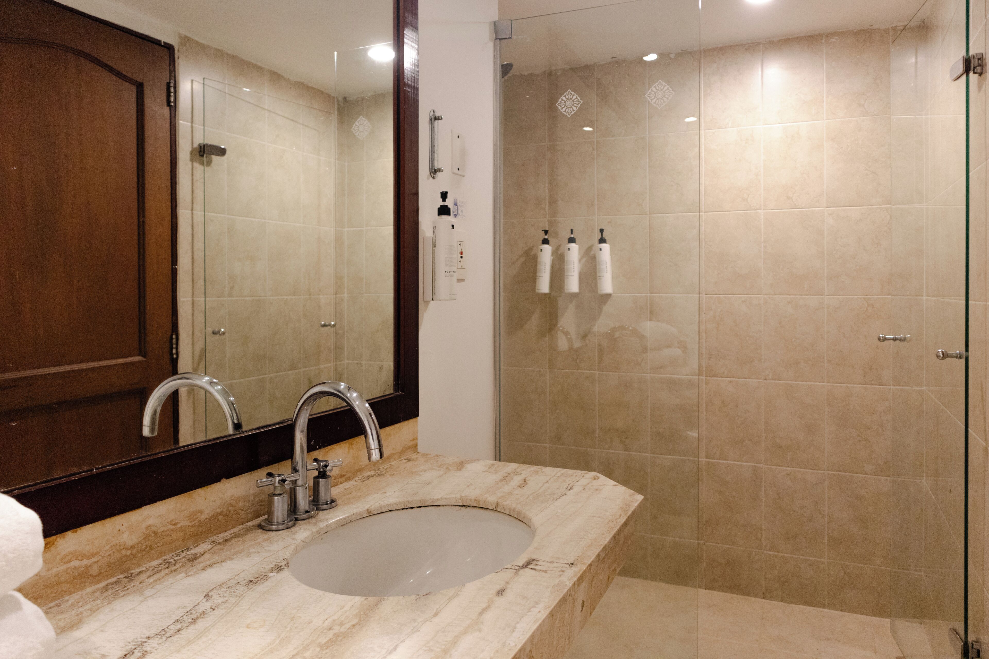 Un baño con lavamanos de mármol, espejo, cabina de ducha con mampara y artículos de aseo en la pared.