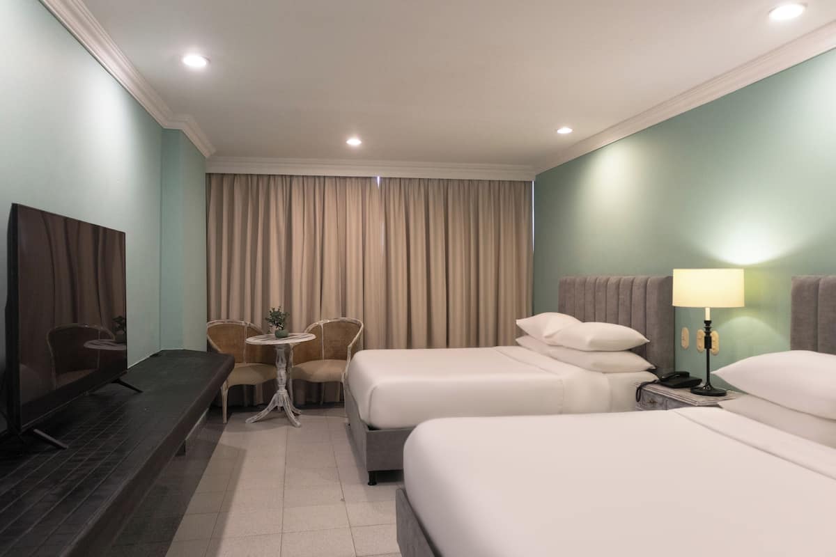 Une chambre d’hôtel avec deux lits, un bureau, une chaise, une télévision et une lampe.