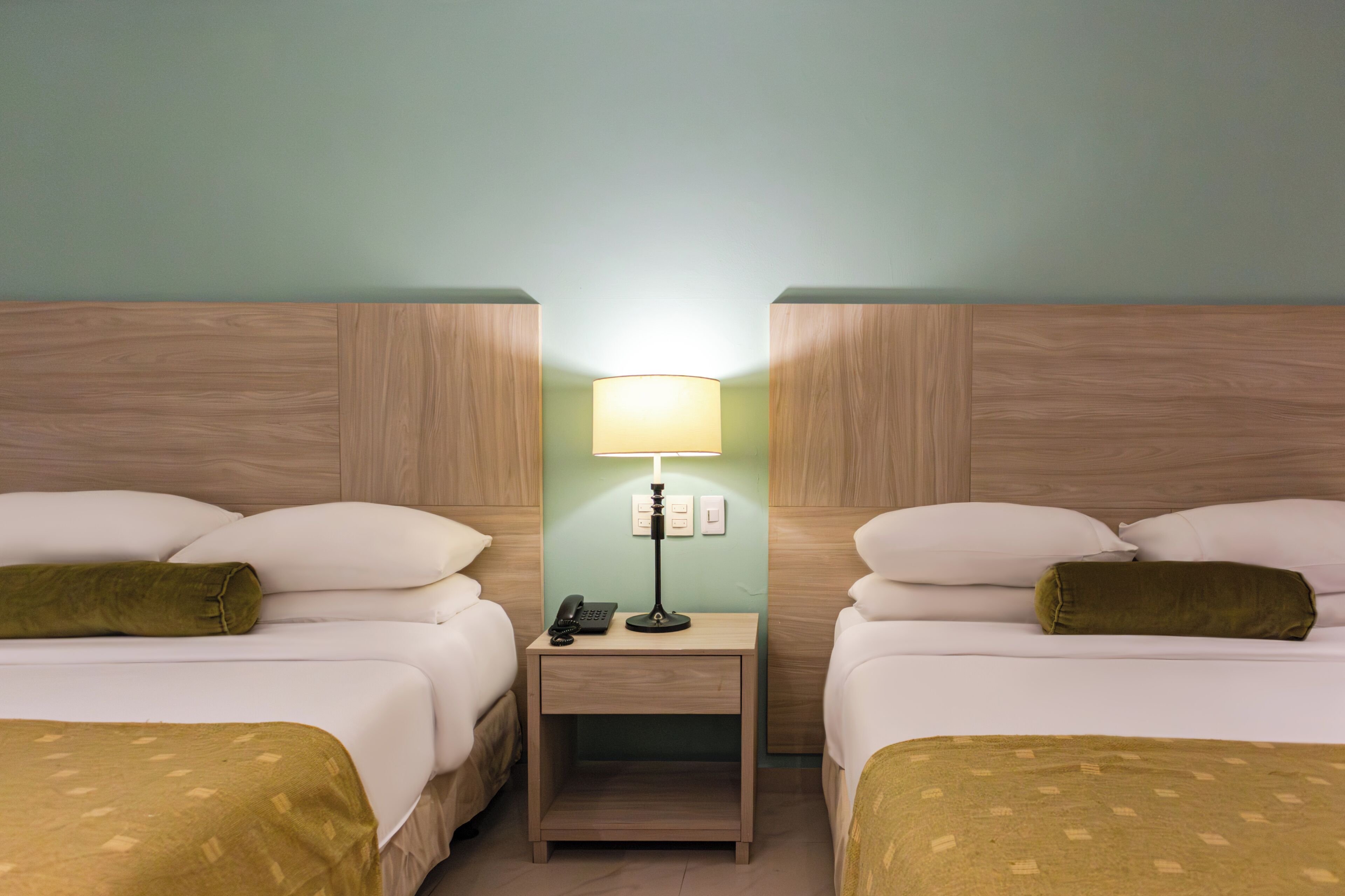 A hotel room with two beds, a nightstand with a lamp, and a phone.