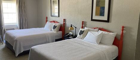 A hotel room with two beds, each with white bedding and red headboards. There is a framed picture on the wall above each bed.