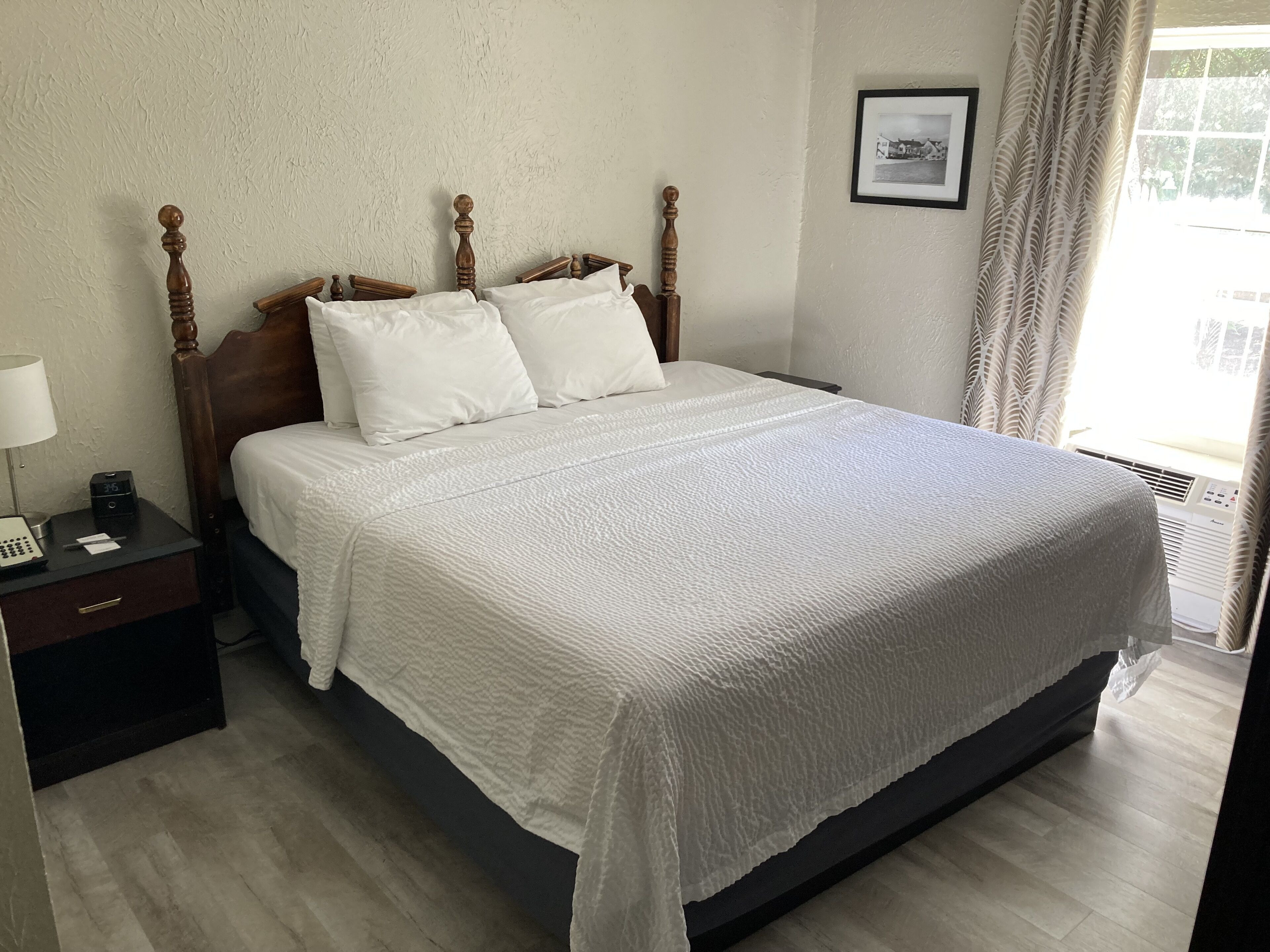 A neatly made bed with a textured white bedspread, a wooden headboard, and a nightstand with a lamp and a clock.