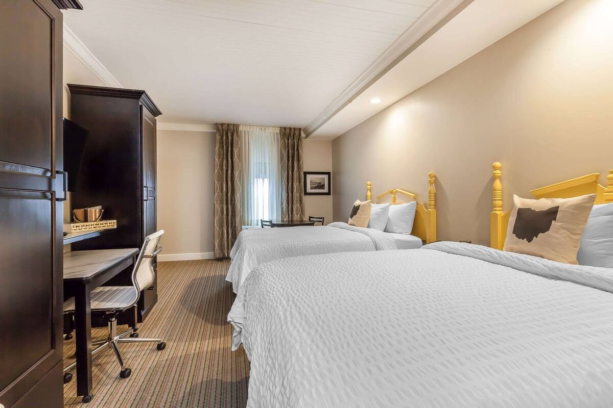 A hotel room with two beds, a desk with a chair, a television, and a framed picture on the wall.