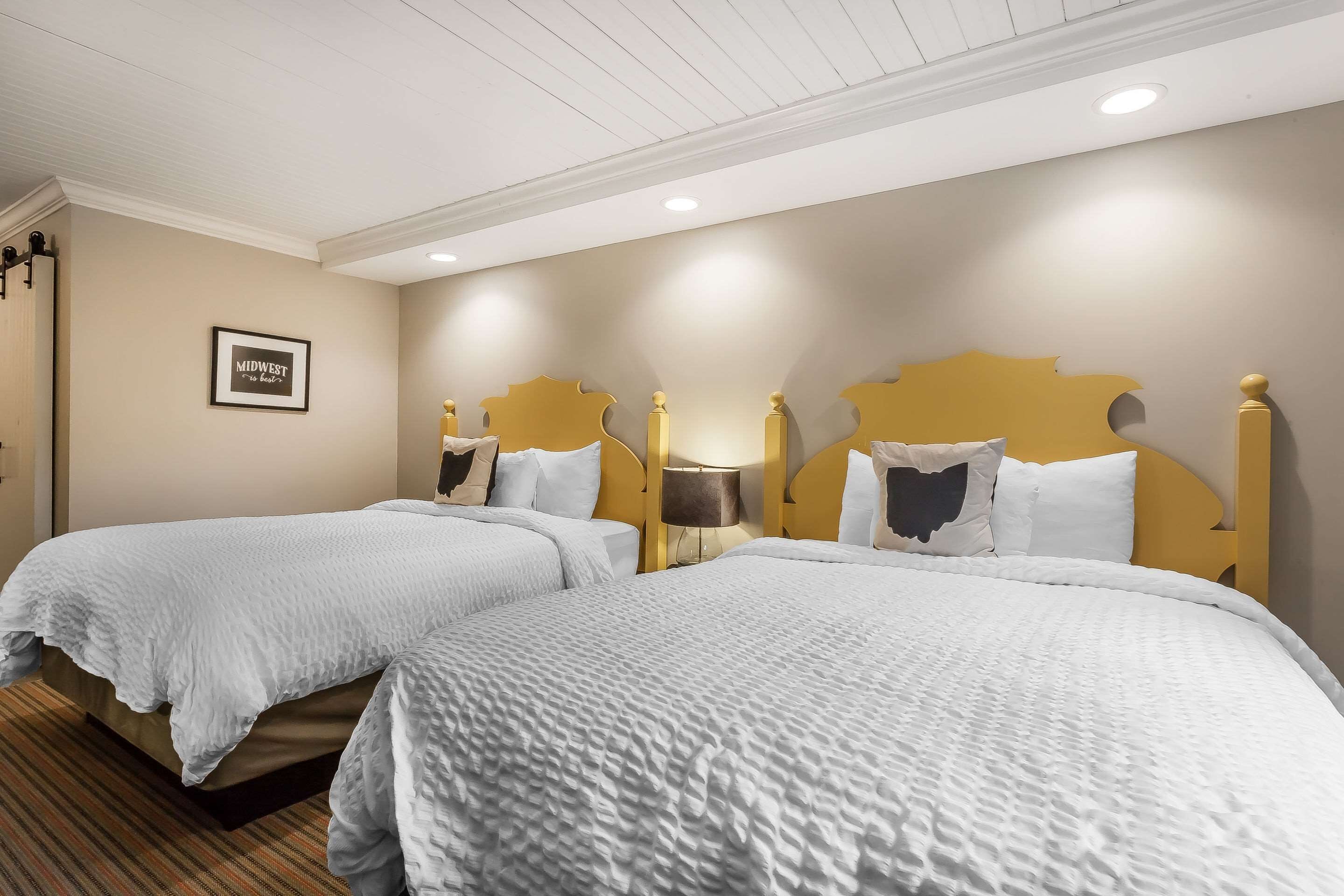 Une chambre d’hôtel avec deux lits, des murs de couleur beige et un panneau encadré accroché au mur.