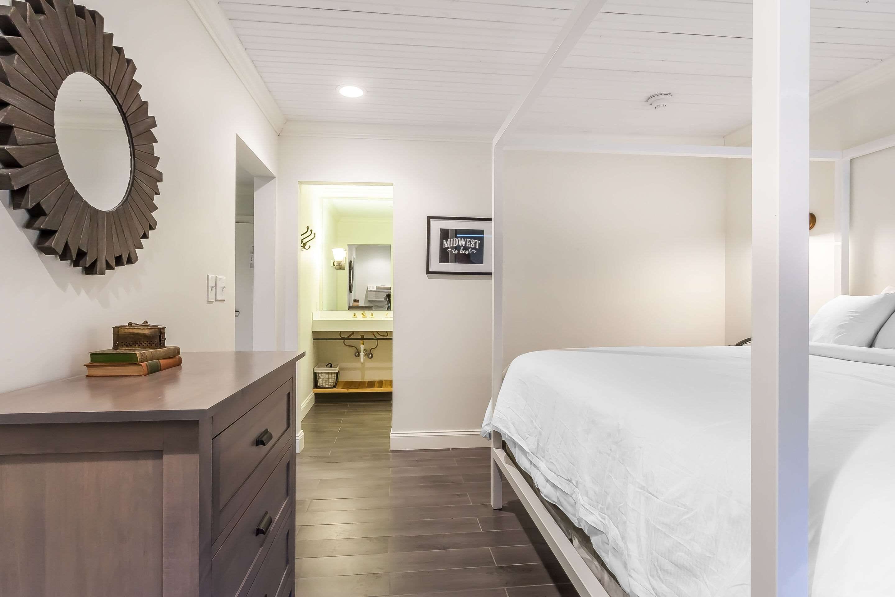 Een slaapkamer met een bed, een dressoir, een spiegel en een bord met tekst op de muur.