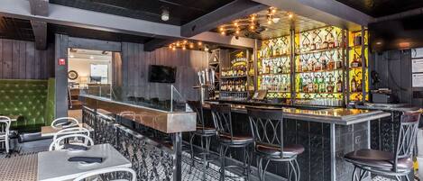 Una zona de bar con mostrador, taburetes y una variedad de botellas.