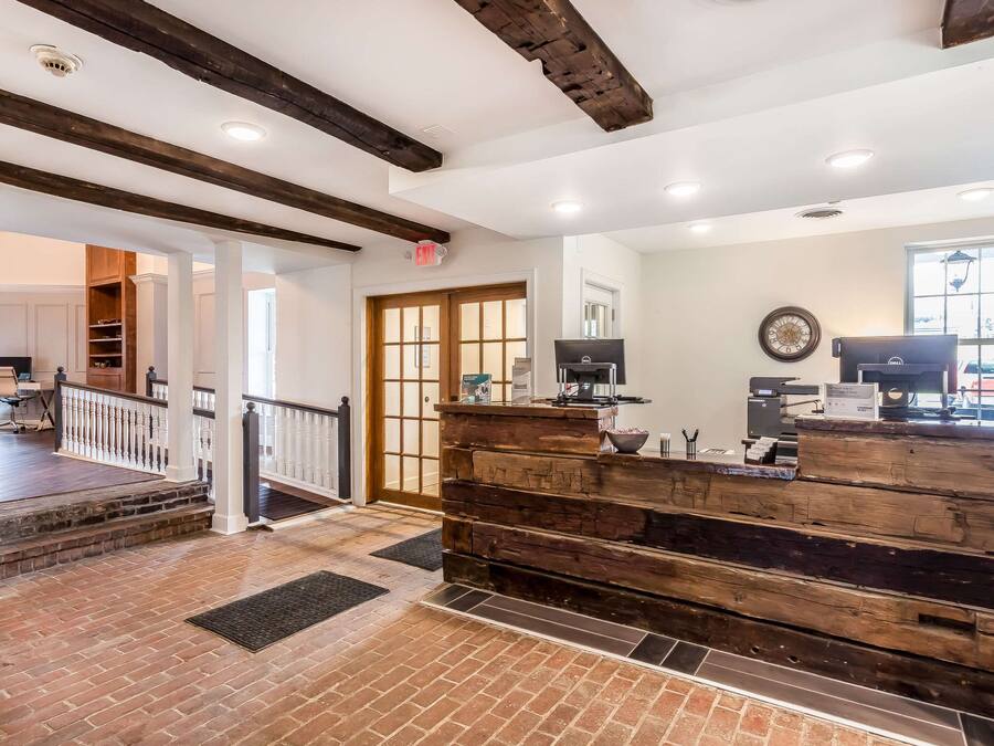 A reception area with a wooden counter, a staircase leading to another room, and a large window with natural light.
