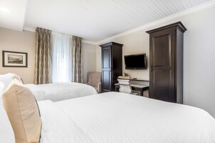 Habitación de hotel con dos camas, un escritorio con silla, un televisor y un armario.