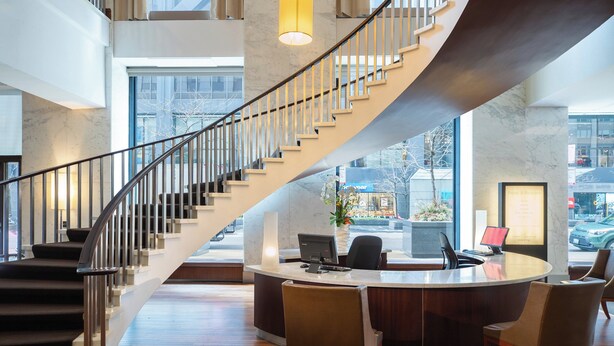 A modern hotel lobby with a central reception desk, a curved staircase, and a view of the street through large windows. - The Westin Michigan Avenue Chicago (Chicago)