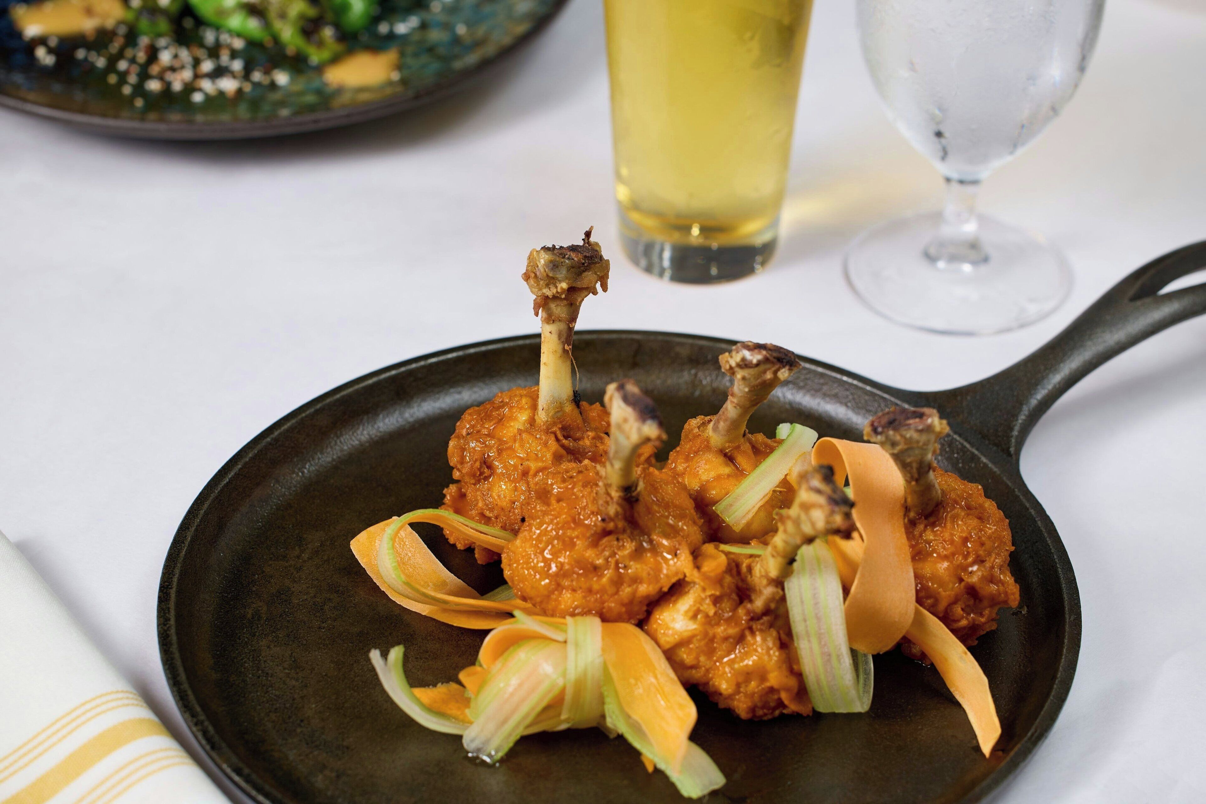 A skillet with fried chicken wings and celery on a plate.