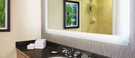 A modern bathroom with a large mirror, a sink, and a shower.
