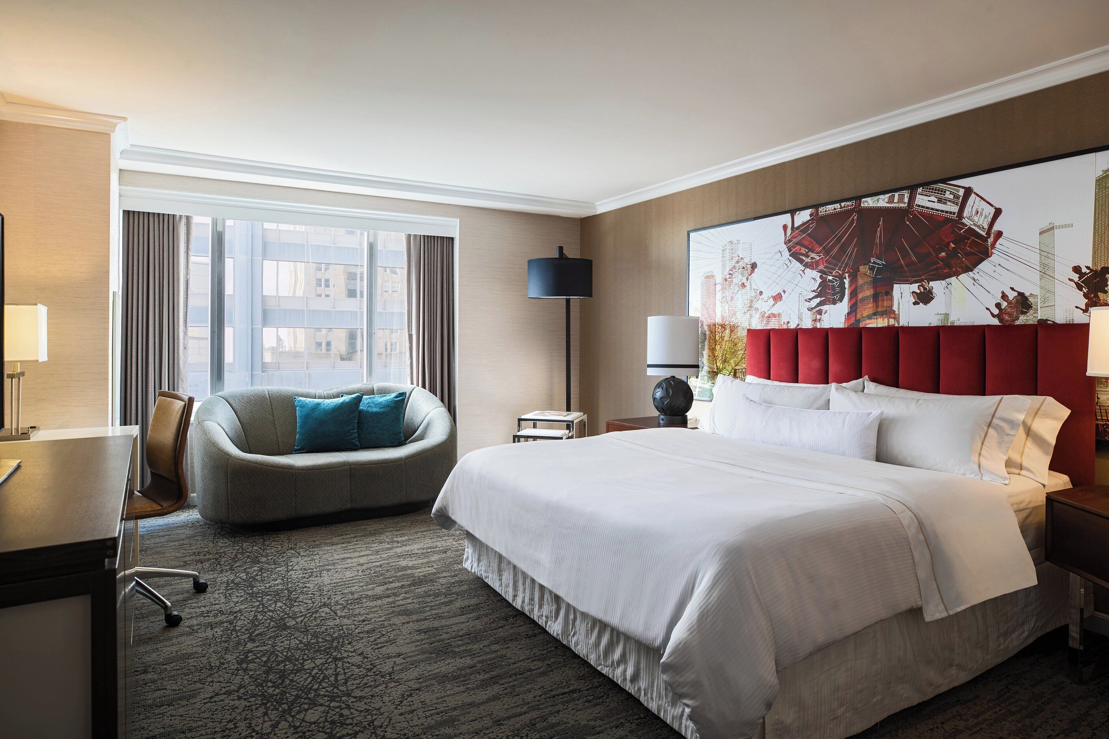 Een hotelkamer met een groot bed, een bureau, een stoel, een raam met gordijnen en een wandlamp.