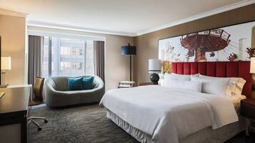 Een hotelkamer met een groot bed, een bureau, een stoel, een raam met gordijnen en een wandlamp.